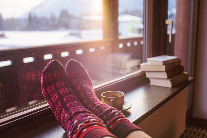 Feet in woollen socks by the Alps mountains view. Woman relaxes by mountain view with a cup of hot drink. Close up on feet. Winter and Christmas holidays concept.