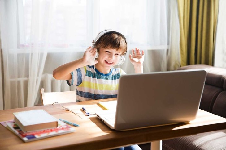 child boy in headphones is using a laptop and study online with video call teacher at home. homeschooling, distant learning