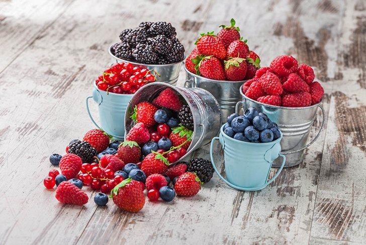 Berries mix blueberry, raspberry, red currant, strawberry, in five old tin cans spilled on white rustic wooden table in studio