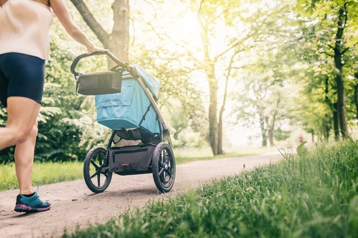 Running woman with baby stroller enjoying summer day in park. Jogging or power walking supermom, active family with baby jogger.