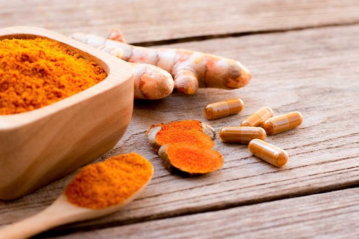 Turmeric ( curcumin, Curcuma longa Linn) powder capsules and tumeric ground in wooden bowl and spoon isolated on wood table background.