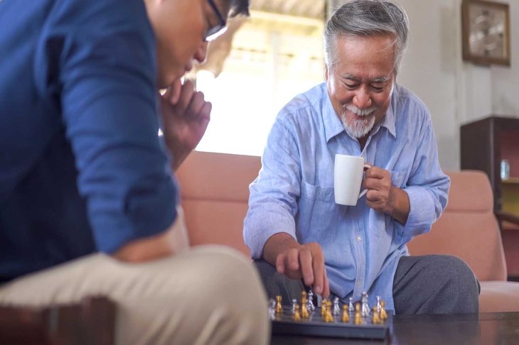 Asian Senior man playing chess with son at home