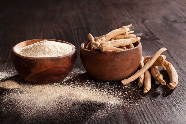 Ashwagandha powder and roots in wooden cups on black background. Superfood, adaptogen, nutritional supplement.